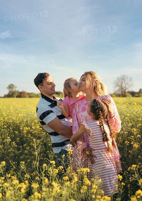 A heartwarming moment as a mother receives kisses from her children while the father lovingly embraces them. The golden light enhances this tender and emotional family connection