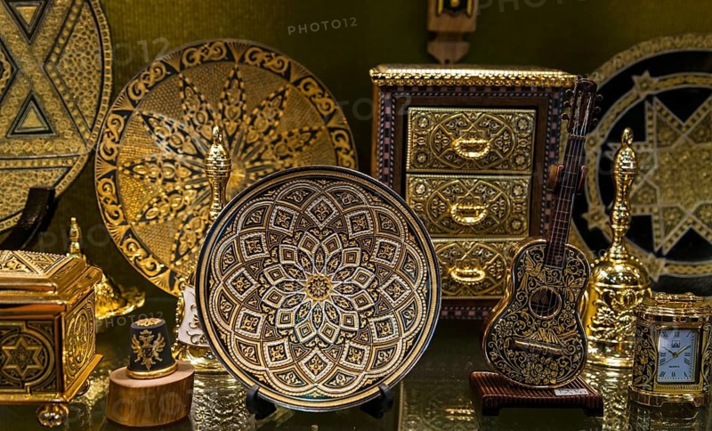 A collection of gold-decorated decorative objects, including plates and caskets with complex patterns and symbols on stands, Toledo, Castilla-La Mancha, Spain