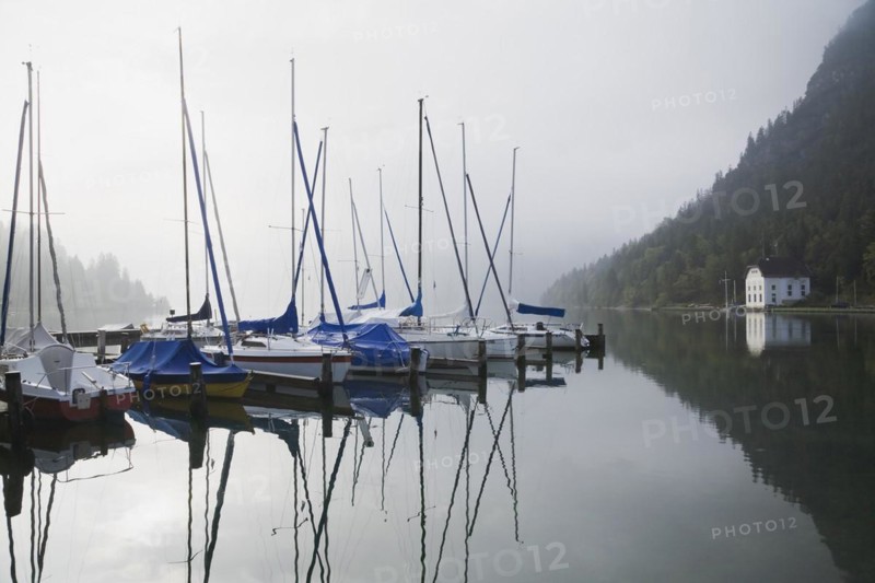 Sailboats moored at marina on Lake Plansee through misty early morning sunrise, Tyrol, Austria