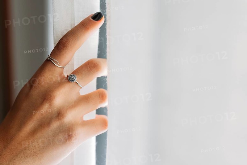 Closeup view of anonymous woman hand with rings opening the curtains