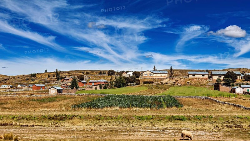 Green and brown fields with small houses under a lively sky, the villages and countryside near Puno in Peru