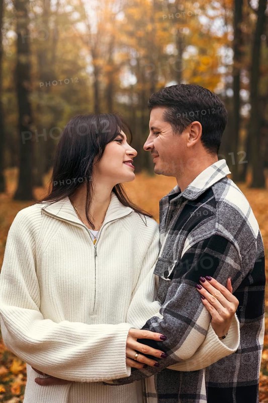 A couple shares a joyful embrace surrounded by vibrant autumn foliage in a serene forest. The warm colors of the leaves create a romantic and cozy atmosphere