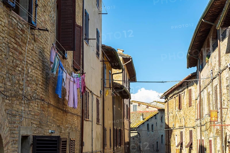 Street with typical houses with shutters, laundry drying in front, San Gimignano, Tuscany, Province of Siena, Italy