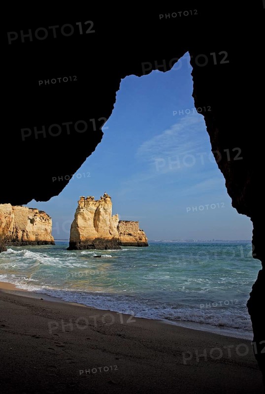 Praia do Pinhao, Lagos, Algarve, Portugal, View from a cave onto rocks in the sea with blue sky and waves on the sandy beach