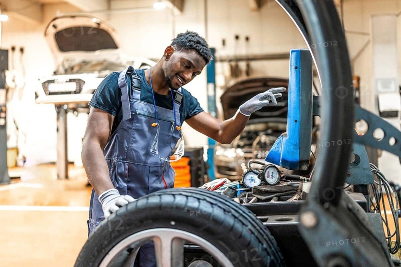 Young smiling afro american mechanic changing car tire using digital tyre changer machine in a car repair shop