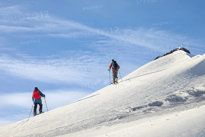 Two skiers ascend a snowy slope under a clear blue sky, showcasing the thrill of ski touring in a pristine winter landscape. Perfect for winter sports enthusiasts and adventure seekers