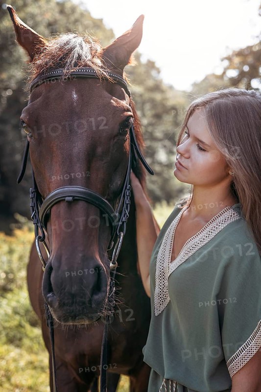 A young girl stands beside a horse in a sunlit forest, displaying a tranquil relationship. The scene captures a serene moment of connection with nature and equine beauty