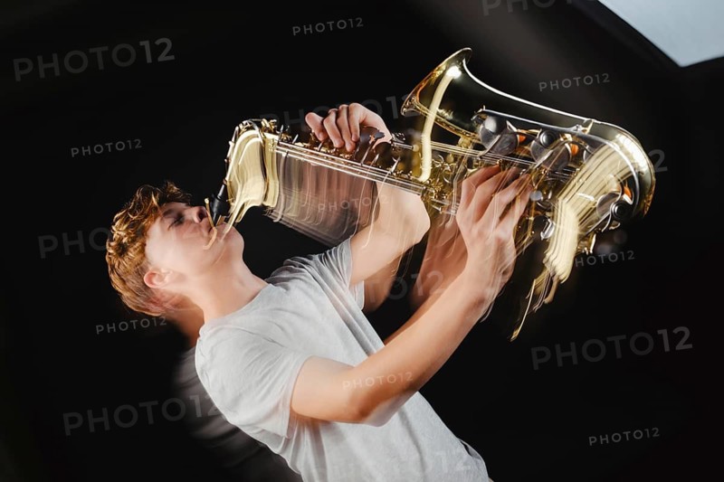 A teenage boy is captured in a dramatic pose while playing a saxophone against a black background in a studio setting, highlighting his focus and enjoyment