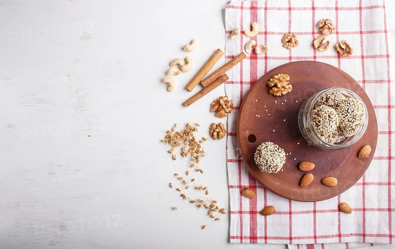 Energy balls cakes with almonds, sesame, cashew, walnuts, dates and germinated wheat on wooden board in glass jar, top view, copy space