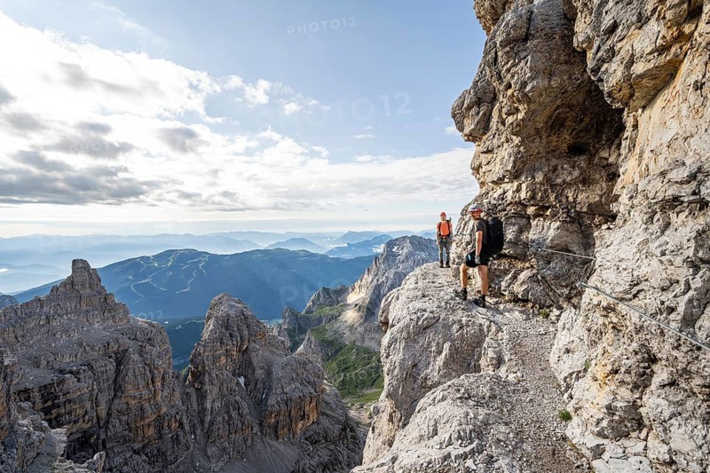 Two mountaineers climb an exposed rock band in the secured Via Ferrata Bocciere Centrale via ferrata, Brenta Mountains, Parco Naturale Brenta-Adamello, Trentino, Italy