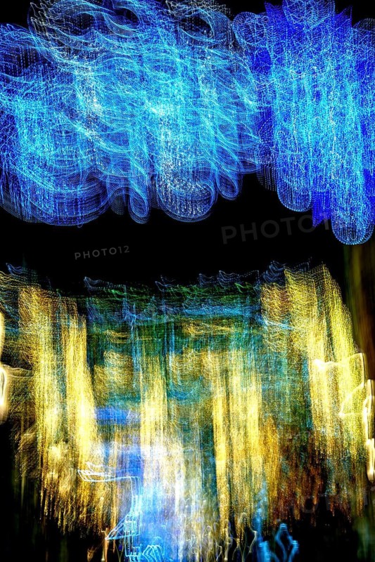 Soft, swirling colors form an abstract landscape of blue and gold lights against a dark background, capturing the dynamic energy of a lively urban setting during the evening