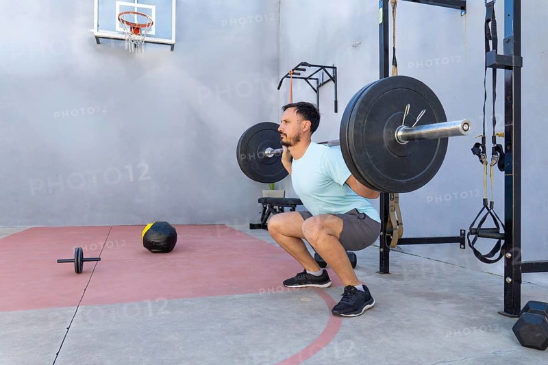 Focused athlete executing barbell squats in an outdoor gym setting, demonstrating strength and unwavering dedication to fitness while embracing an active lifestyle