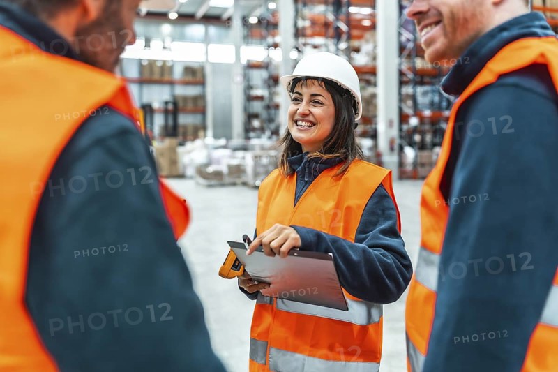 Warehouse workers are smiling and discussing logistics operations, holding a digital tablet with laser scanner