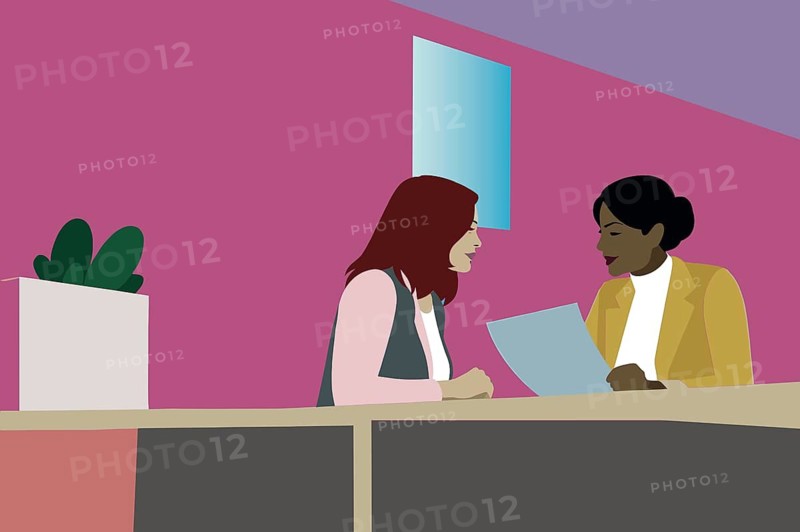Two women engaged in a business discussion at a table in a vibrant office. They appear to be reviewing documents, surrounded by a lively atmosphere