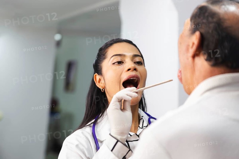 A female doctor performs a routine medical examination on an elderly male patient, assessing his throat with professional care and precision in a clinical setting