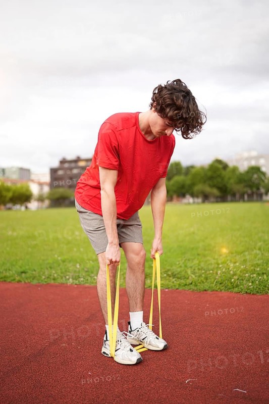 Vertical photo of a young caucasian man warming up with resistance elastic band outdoors in a running track