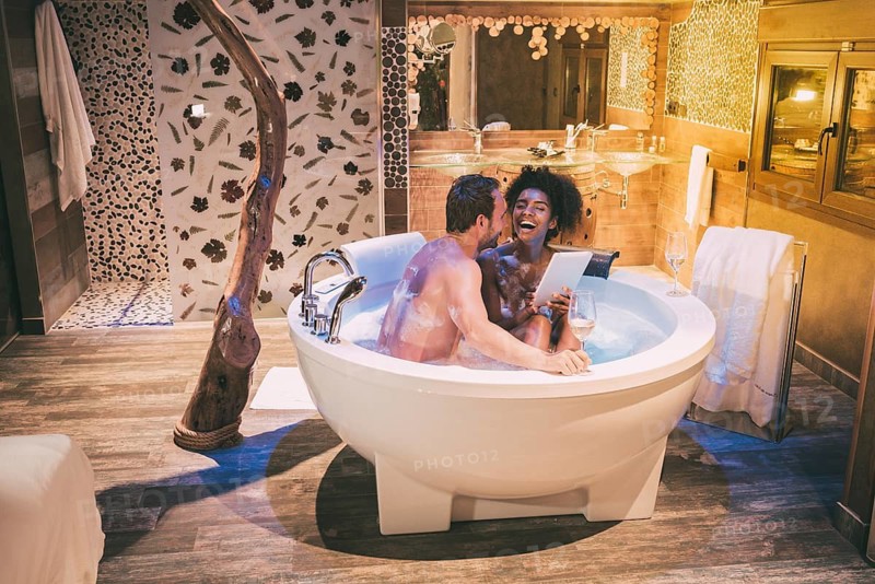 Happy young interracial couple relaxed enjoying their self in the jacuzzi drinking wine and with a tablet