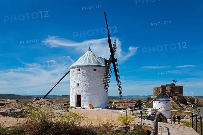 A white windmill in a sunny, rural landscape under a bright blue sky with a few clouds, Consuegra, Toledo, Castilla-La Mancha, Route of Don Quixote, Spain