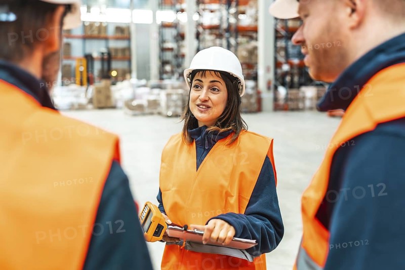 Female supervisor holding barcode scanner and clipboard briefing warehouse workers about their tasks