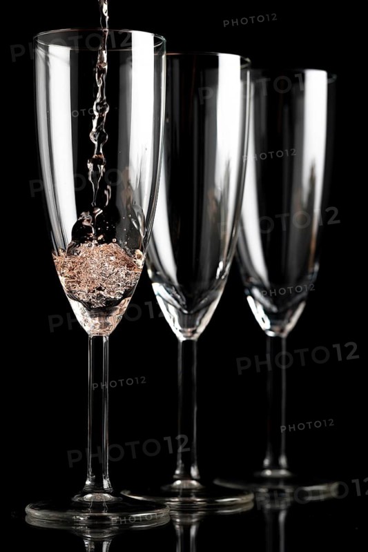 Three champagne glasses in front of a black background, first glass is filled with champagne
