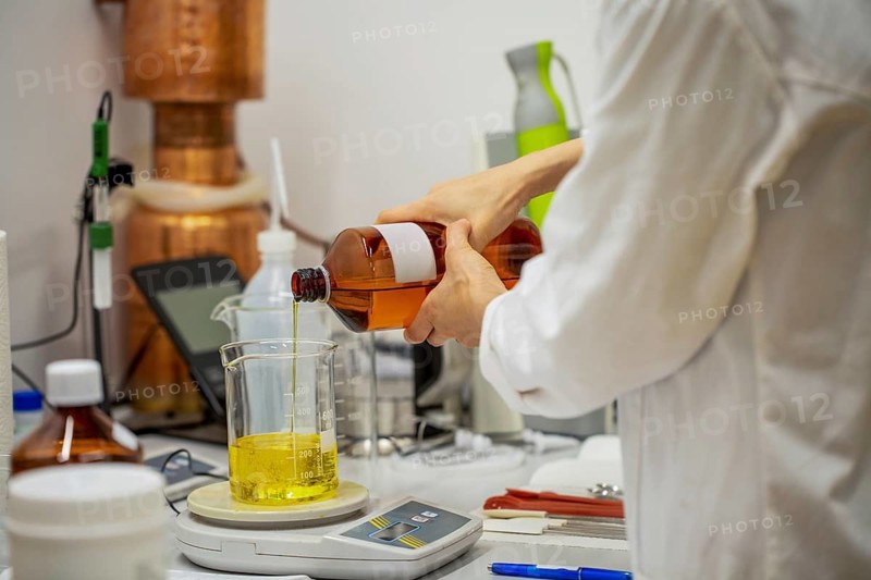 A laboratory setting where natural oil is being poured into a beaker, highlighting the process of crafting natural cosmetic products. Equipment and materials are visible