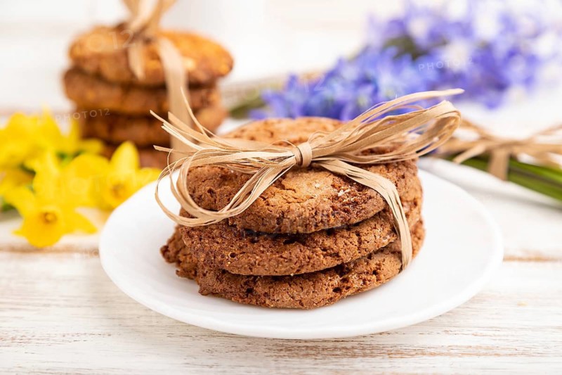 Oatmeal cookies with spring snowdrop flowers bluebells, narcissus and cup of coffee on white wooden background. side view, close up, defocused, still life. Breakfast, morning, spring concept