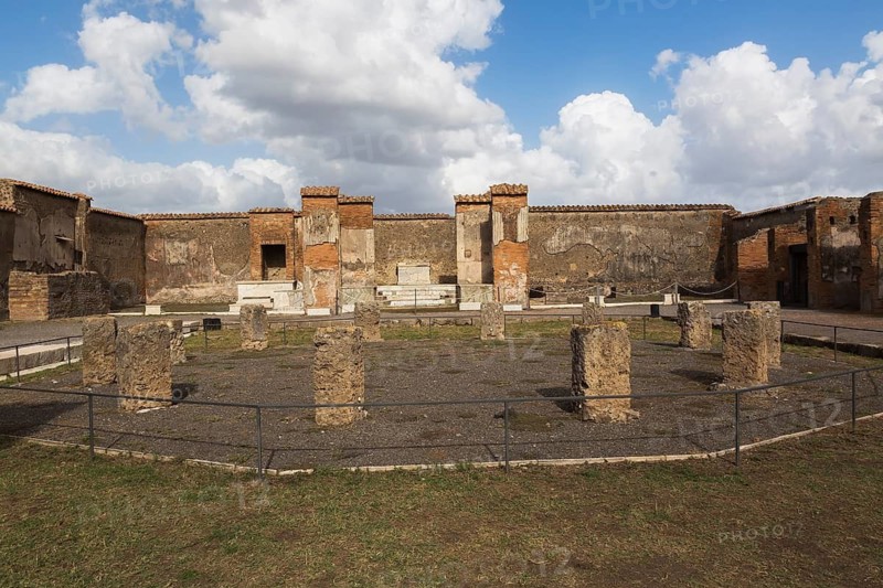 Remnants of old stone columns and terracotta brick and stone walls in a courtyard at the ancient ruins of Pompeii, Campania region, Italy
