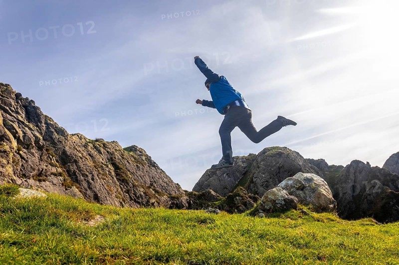 Male hiker jumping between rocks on mount aiako harriak, also known as penas de aia, near oiartzun, gipuzkoa, in the basque country