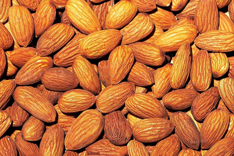 This image captures a detailed close-up of raw almonds with visible textures and natural tones, filling the frame completely