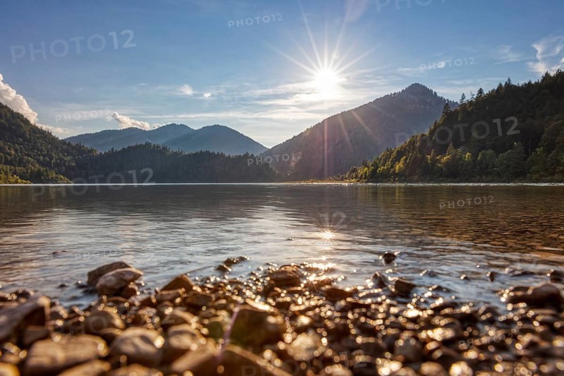 Peaceful lake with mountain backdrop, golden sky and sunlight on water and stones, Weitsee