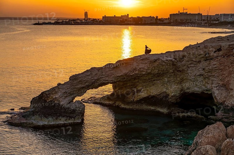 Young woman on the natural rock bridge Love Bridge in the sunset, Agia Napa, Cyprus