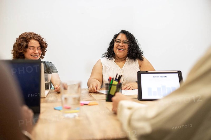 A multiracial group collaborates at a coworking space, engaging in a lively discussion. Laptops and tablets are present, adding a touch of modern technology to their meeting
