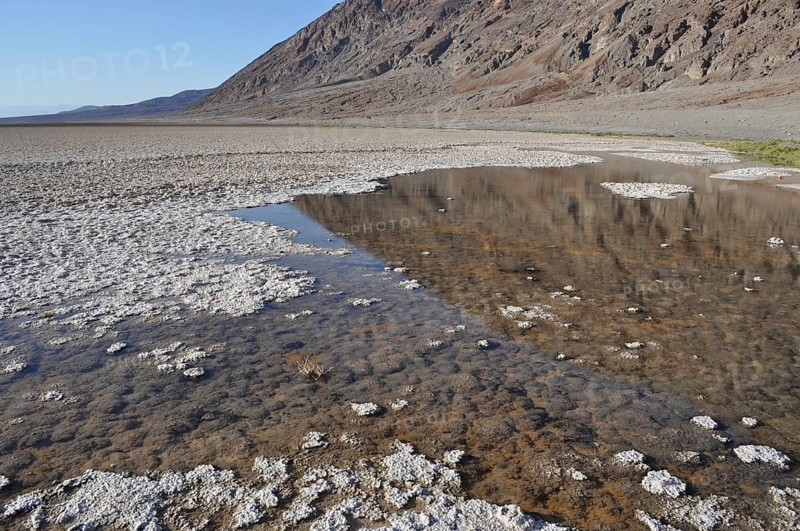 Salty area with a small area of water reflecting mountains in the background, Badwater Basin, Death Valley National Park, Mojave Desert, California, Nevada, USA