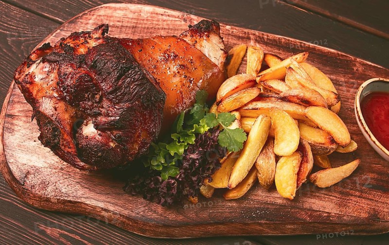 Pork knuckle, in soy-honey sauce, with fried potatoes, on a wooden chopping board, homemade, no people