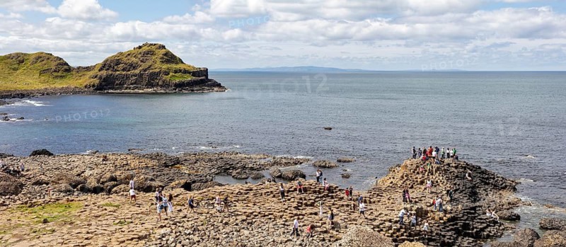 People climb basalt columns on the coast with a view of the sea, Giant Causeway