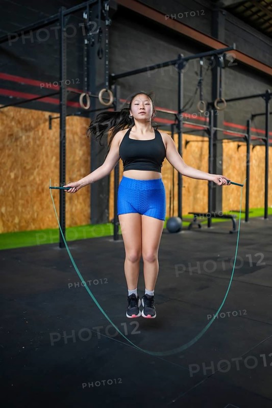 Vertical full length and frontal portrait of an Asian sportswoman jumping rope in a cross training gym