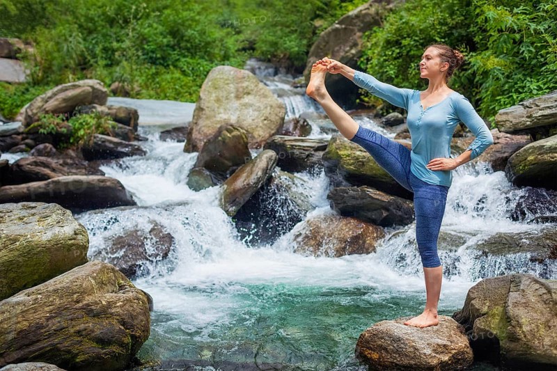 Yoga outdoors, woman doing Ashtanga Vinyasa Yoga balance asana Utthita Hasta Padangushthasana, Extended Hand-To-Big-Toe Pose position posture outdoors at waterfall