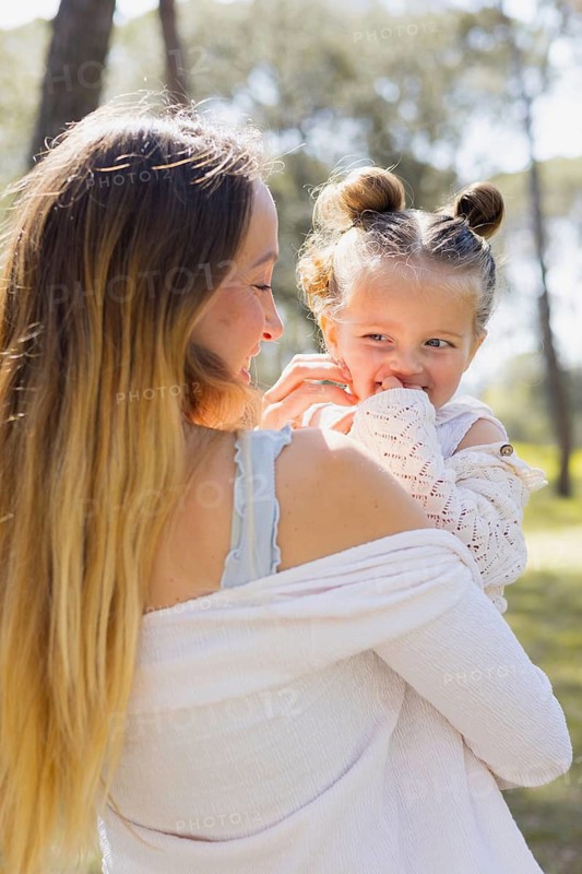 A pregnant woman shares a joyful moment with her daughter outdoors. Embracing nature, they enjoy a sunny day together, expressing warmth and family bonding