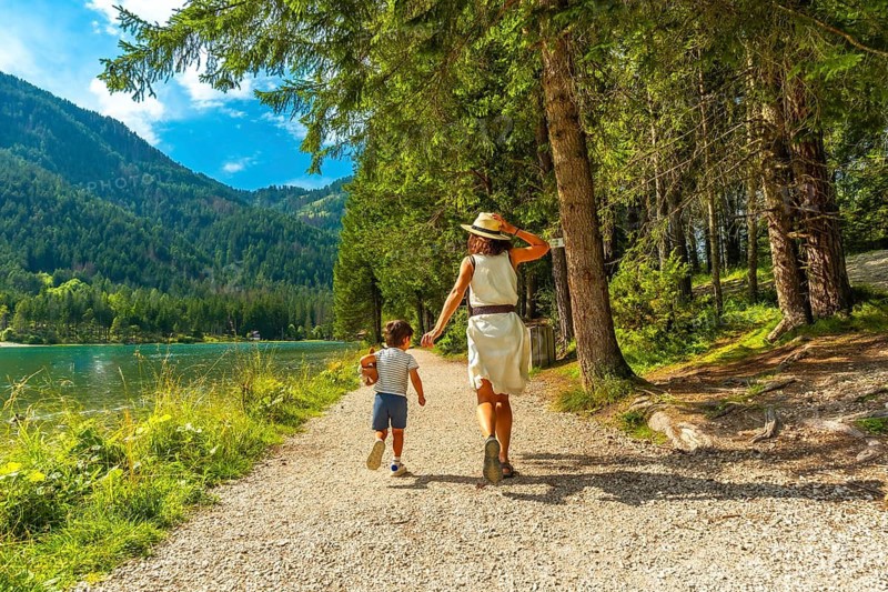 Mother and son enjoying a walk along the scenic shores of lake dobbiaco, surrounded by the stunning beauty of the dolomites in summer