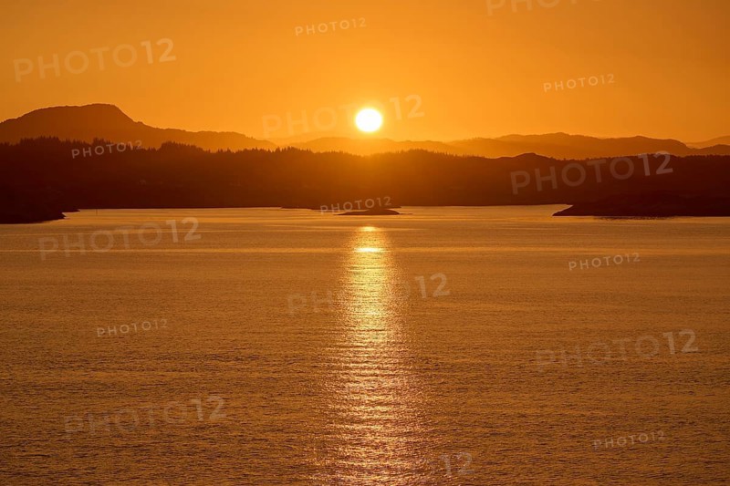A soft orange sunrise behind the dark silhouettes of mountains and a calm sea, autumn, Bergen, North Sea, Norway