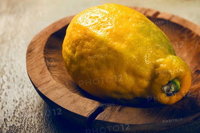 A vibrant lemon sits on a rustic wooden plate. The soft lighting accentuates its texture and color, creating a warm atmosphere in a home kitchen