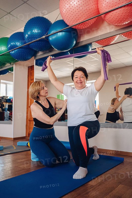 Elderly woman participate in a gym workout session, guided by a professional instructor, focusing on strength and flexibility. Aimed at improving health and community support