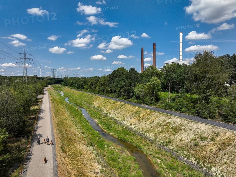 Bottrop, North Rhine-Westphalia, Germany, Renaturalised Boye, the tributary of the Emscher, was transformed into a near-natural watercourse, flood protection through newly designed floodplains, the Boye is now free of wastewater after the construction of a parallel sewer, is part of the Emscher river system and thus part of the Emscher conversion, was previously an open, above-ground wastewater channel, mixed water channel with surface water and wastewater. Wind turbine on Mottbruch spoil tip at the back. On the right, industrial area with chimneys on Essen territory
