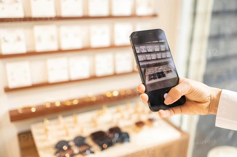 A person is taking a photo with a smartphone in a stylish bag store, capturing the elegant display of various products on shelves. Perfect for modern retail concepts