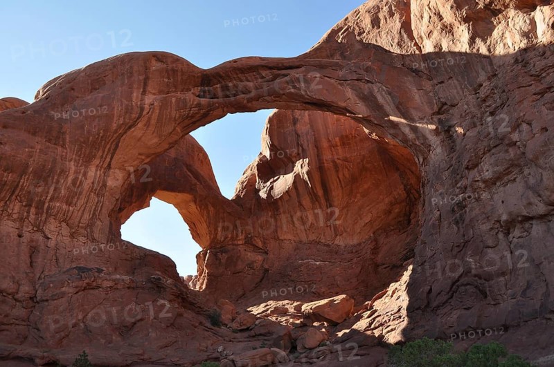 Massive double arch, called Double Arch, made of rocks under clear blue skies in a desert-like area, Arches National Park, Utah, USA