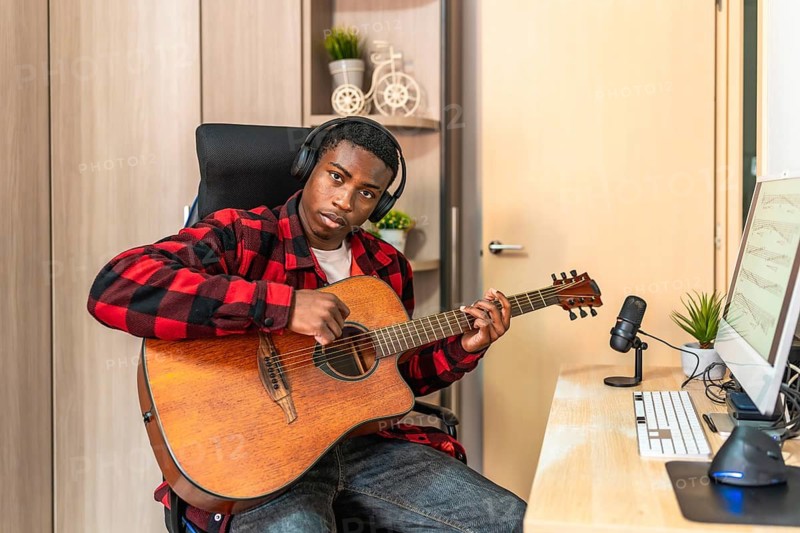 Young man playing guitar and recording music at home studio using professional microphone and computer