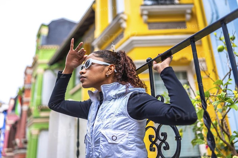 Side view of a beauty young modern african american woman covering eyes to look forward outdoors standing next to colorful facades