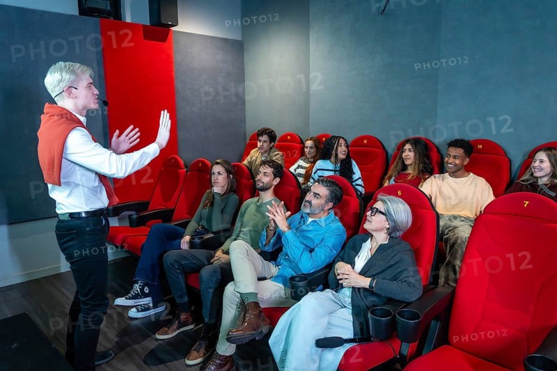 Enthusiastic speaker with microphone presenting a movie to a diverse audience in a modern cinema, fostering engagement and discussion