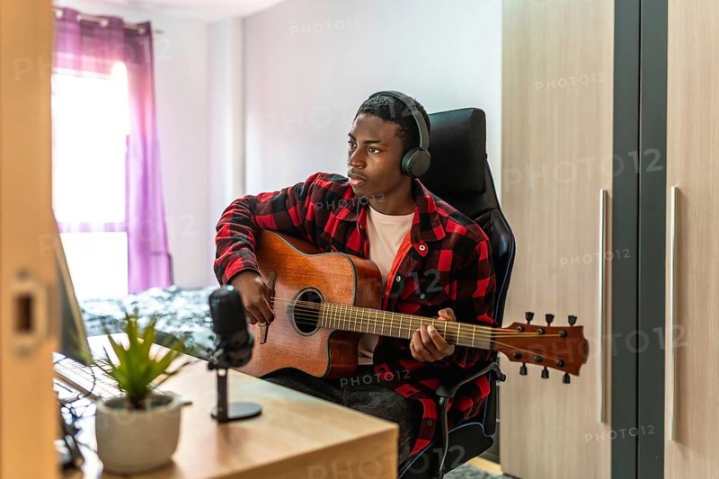 Young man playing acoustic guitar and recording music at home studio using a computer, microphone and headphones