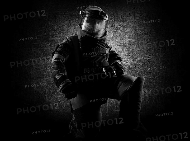 Military man in a protective sapper suit is kneeling and is preparing to neutralize the bomb.